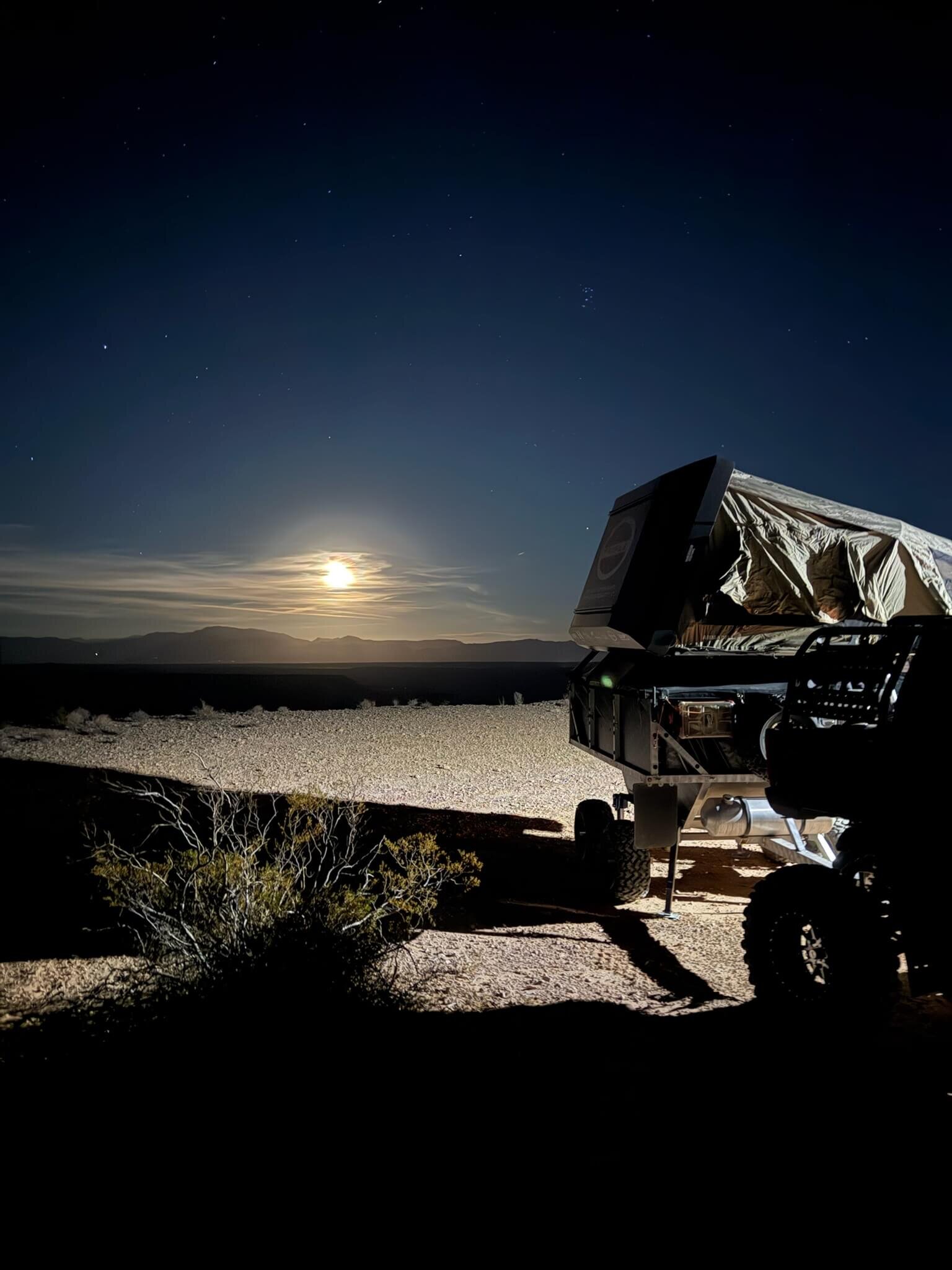Lightweight overland camp trailer with a rooftop tent under a full moon in the desert