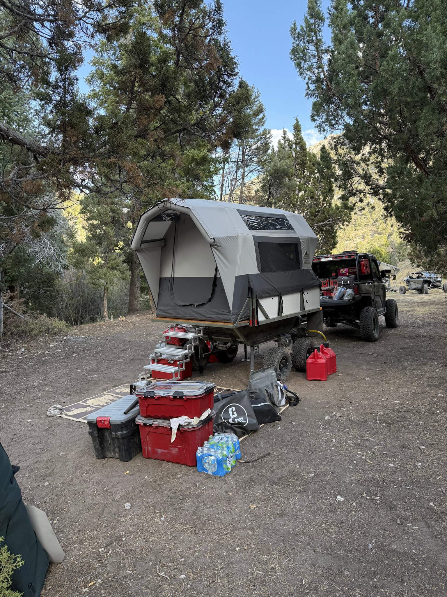 A High Country Unlimited overland camping trailer parked at a high-desert camp behind a side-by-side UTV