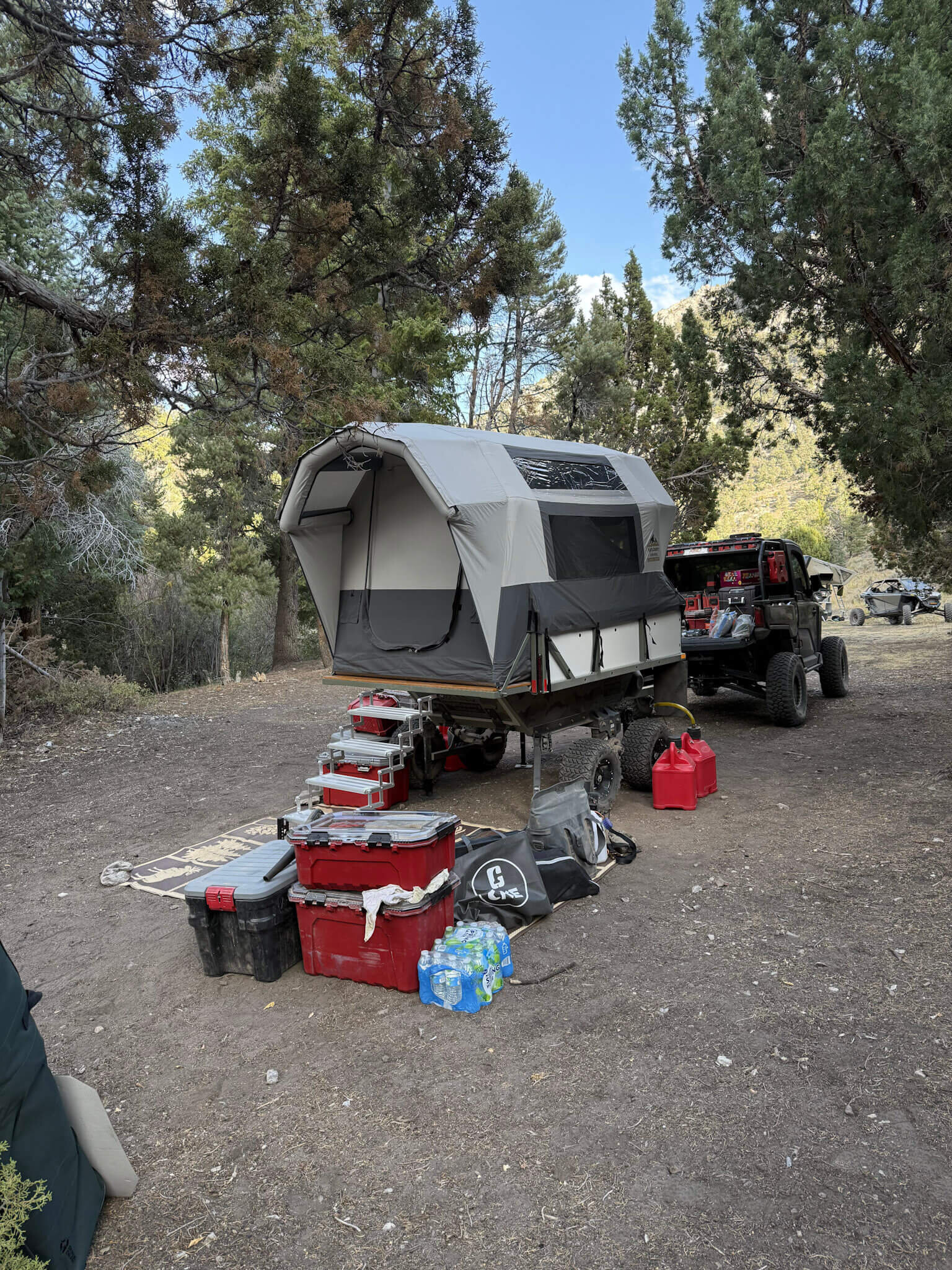 A High Country Unlimited overland camping trailer parked at a high-desert camp behind a side-by-side UTV