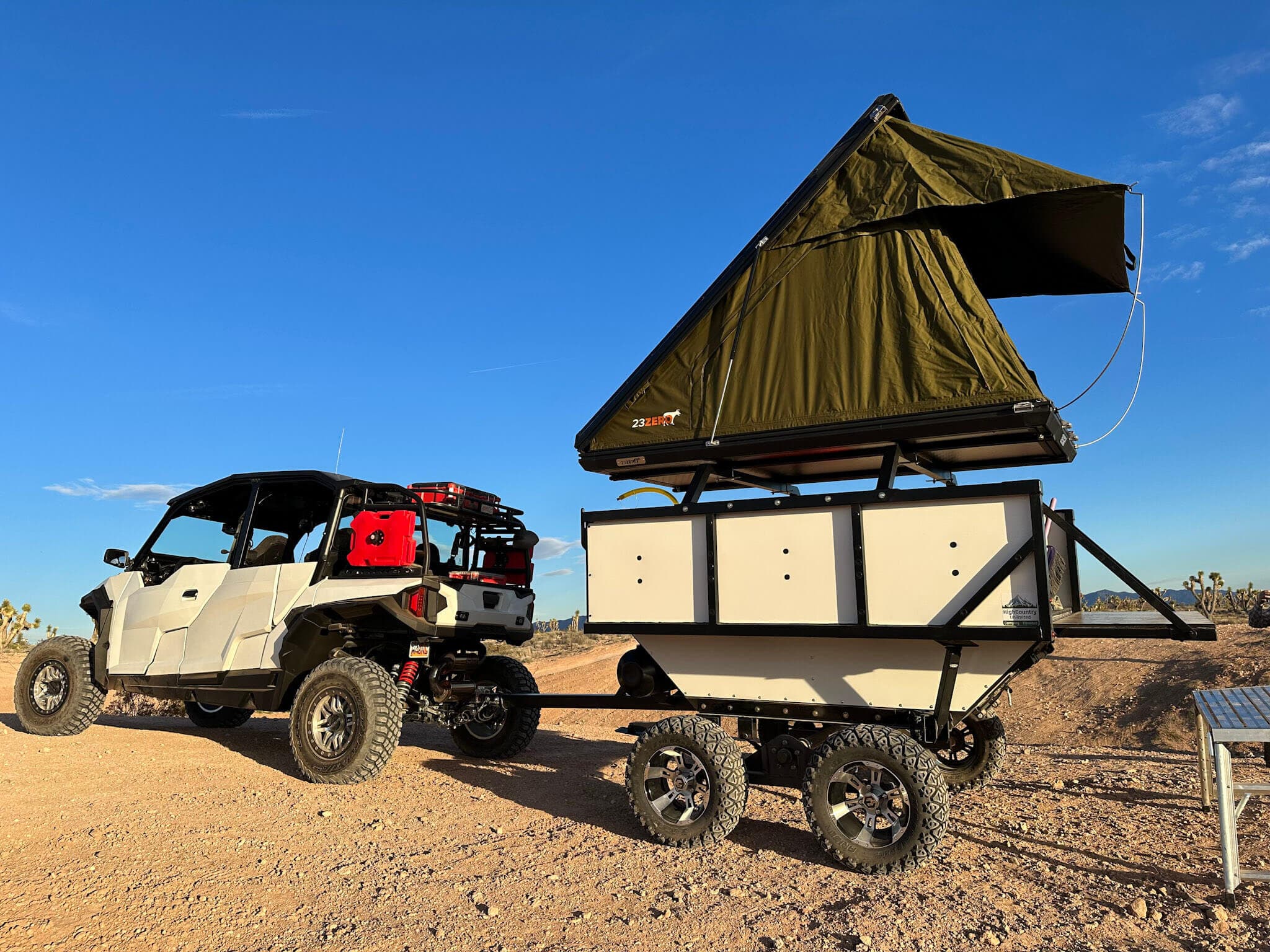 A High Country Unlimited overland camp trailer set up beside a side-by-side UTV in the desert