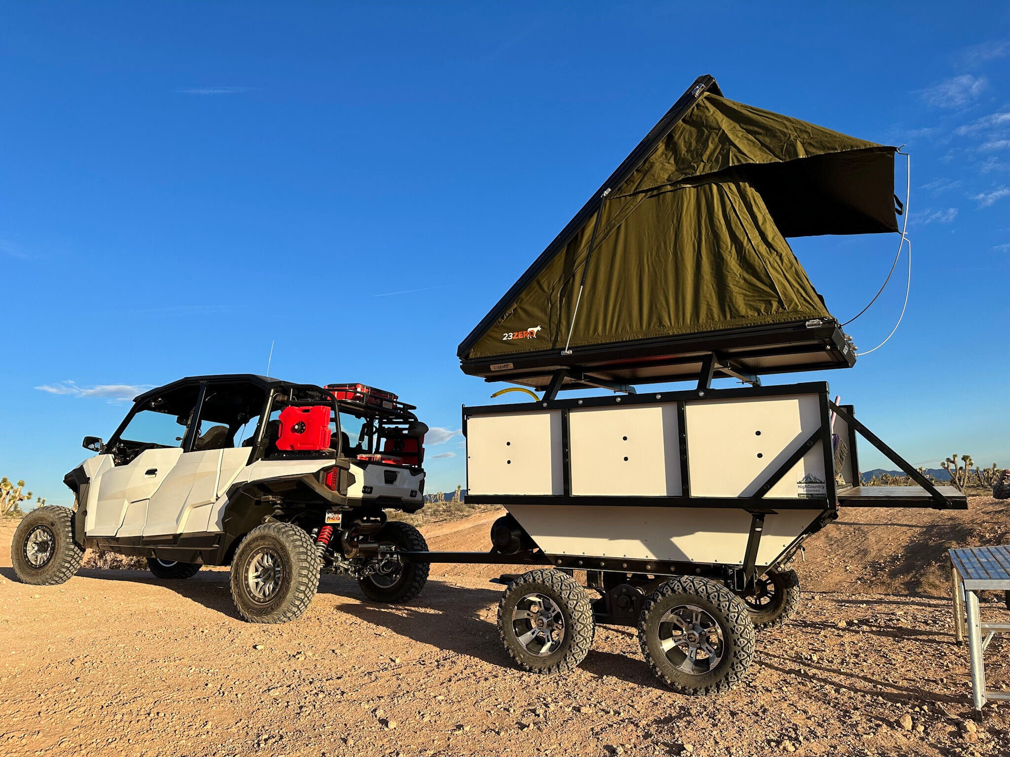 A High Country Unlimited overland camp trailer set up beside a side-by-side UTV in the desert
