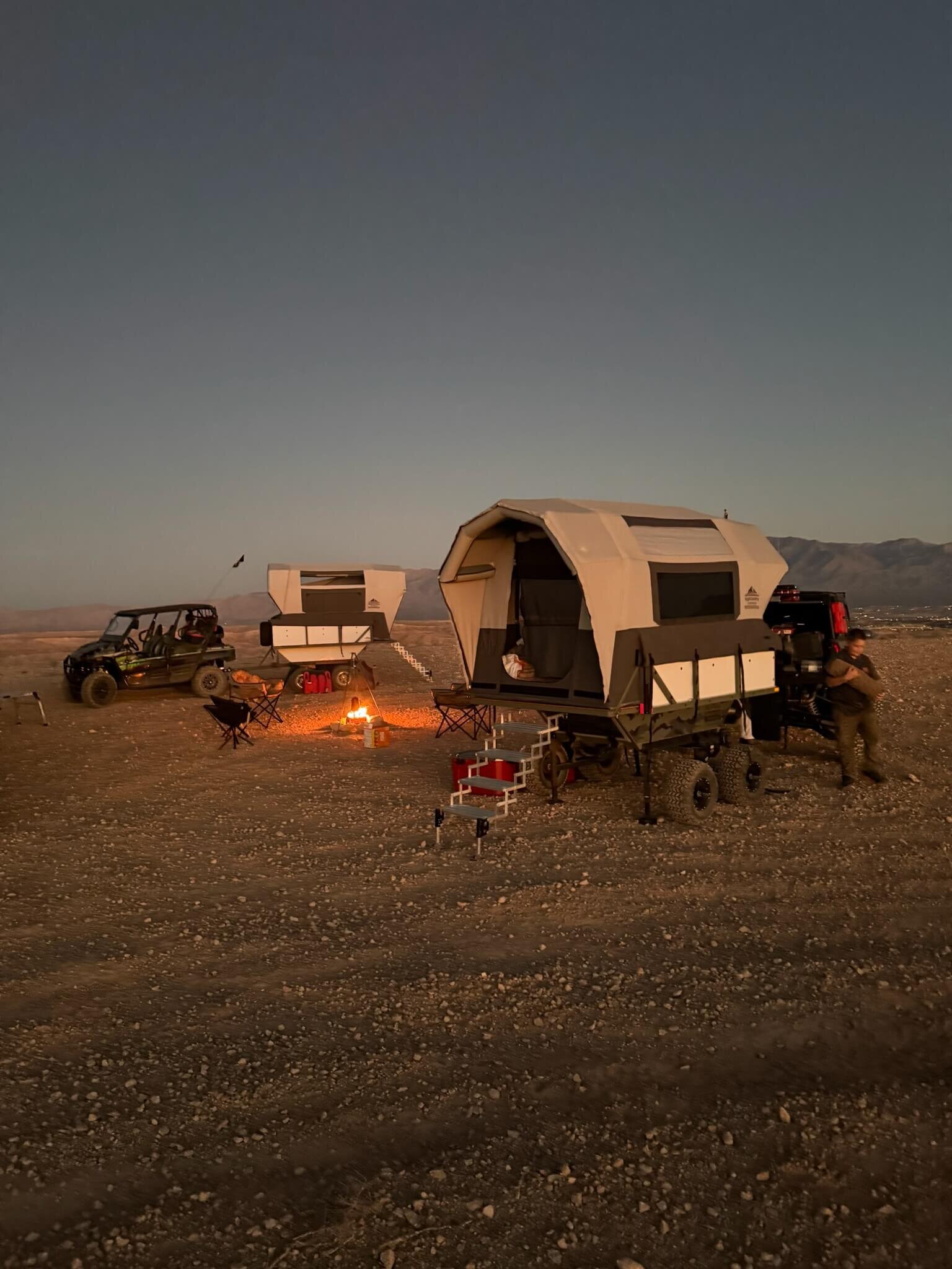 Two High Country Unlimited overland camping trailers set up around a fire at dusk in the Nevada desert